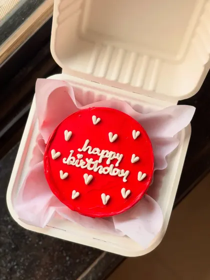 A bold and beautiful red bento cake with "happy birthday" written in white cursive, surrounded by tiny white hearts. It's a simple yet striking design.