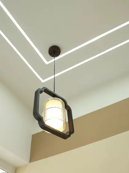 A close-up of a modern pendant light hanging from a false ceiling with profile lighting. This shows our attention to detail in selecting lighting fixtures that complement the overall design.