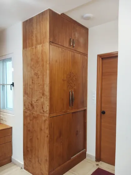 A tall storage unit from the Sampada Home, designed to maximize vertical space. The same carved motif connects it to the rest of the bedroom furniture.