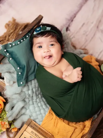 A sweet, tongue-out smile from a newborn baby wrapped in a cozy green swaddle.