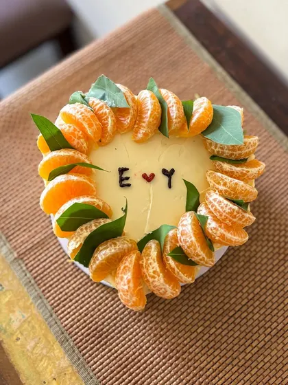 A rustic and minimal heart-shaped cake. It's decorated with a crown of fresh mandarin orange slices and leaves, with simple initials in the center for a personal touch.