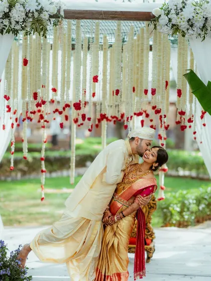 A happy couple shares a playful moment under a canopy of hanging jasmine and rose garlands, capturing the joy of a South Indian wedding.