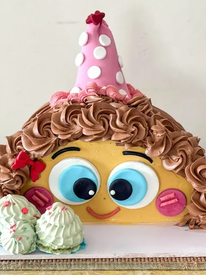 This design features a fun face with a party hat, all made with buttercream and fondant accents.