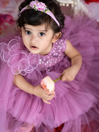 A beautiful portrait of a little girl in a lavender dress, holding a single flower. The soft, dreamy lighting enhances the fairy-tale feel.