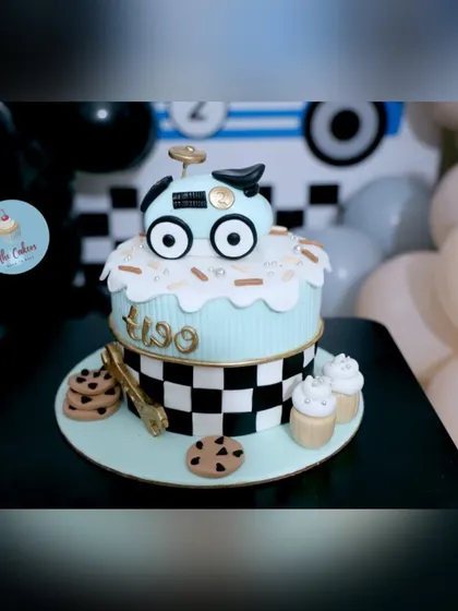 A detailed shot of the two-tier race car cake for Yuvaan's second birthday. The design features a checkered flag pattern, a cute car topper, and coordinating chocolate chip cookie decorations.
