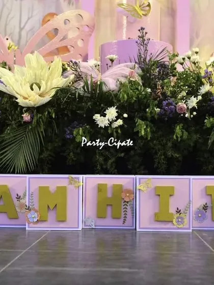 Custom name blocks for Samhita, decorated with floral and butterfly details, placed in front of a stage filled with greenery. Personalization is key to making each event unique.