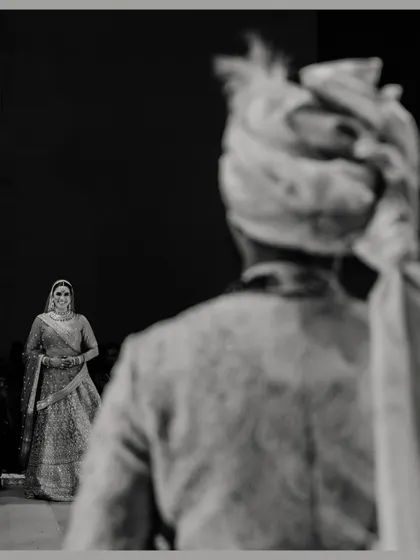 A powerful black and white shot of the groom's first look at his bride. The focus on her approaching figure from his perspective creates a moment of high anticipation and emotion.
