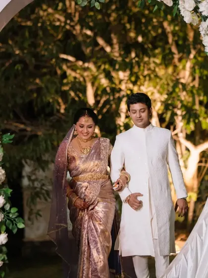 The couple making their grand entrance through a floral arch at their elegant South Indian wedding reception.