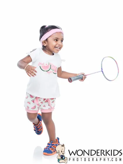 An action shot of a toddler running with a badminton racket. This studio photo against a clean white background perfectly captures the playful energy of a child.