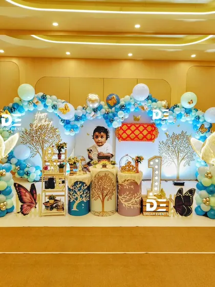 A beautiful butterfly-themed setup for a first birthday, featuring blue and gold tones, illuminated butterfly wings, and a personalized backdrop.