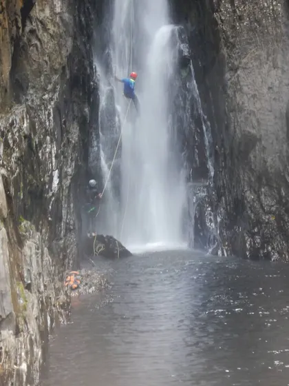 A different angle of the Knotty Canyon rappel, showing the challenging rock formations and powerful water flow.