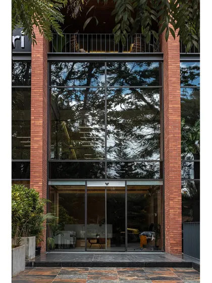The entrance to the Clayworks commercial building, where a double-height glass facade creates a transparent and inviting connection to the street. The reflection of surrounding trees on the glass blurs the line between inside and out.