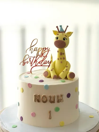 A sweet and simple giraffe-themed cake with pastel polka dots, perfect for a first birthday.