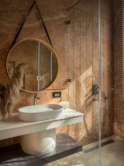 The success of a facade is felt within. In this bathroom at Twin Villa, the exterior screens filter the morning sun, casting gentle, linear shadows across the warm stone. This is how architecture becomes personal, shaping quiet moments and the sensory experience of a home.