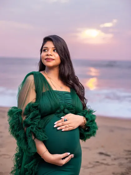 A beautiful solo portrait of the mom-to-be looking out at the horizon, her green gown complementing the soft colors of the sunset.