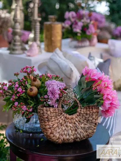 A charming detail from a floral-themed event, where a woven jute bag holds a bouquet of pink flowers. This simple, rustic touch adds texture and warmth to the overall decor.