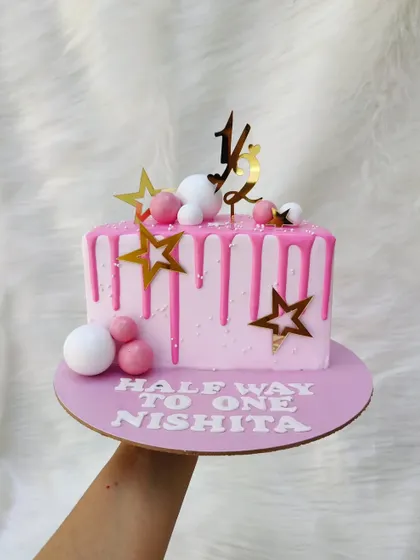 This half-birthday cake is a square shape with a pink drip and star decorations. It's a fun way to celebrate being "halfway to one".