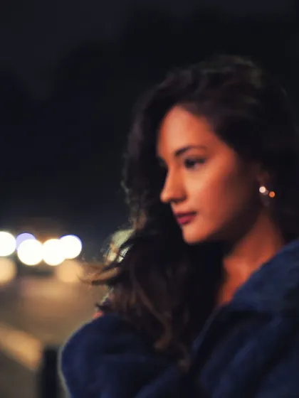 A soft-focus night portrait of a woman in profile, with the blurred bokeh of city lights behind her. The dreamy, out-of-focus quality gives the image a romantic and cinematic feel.