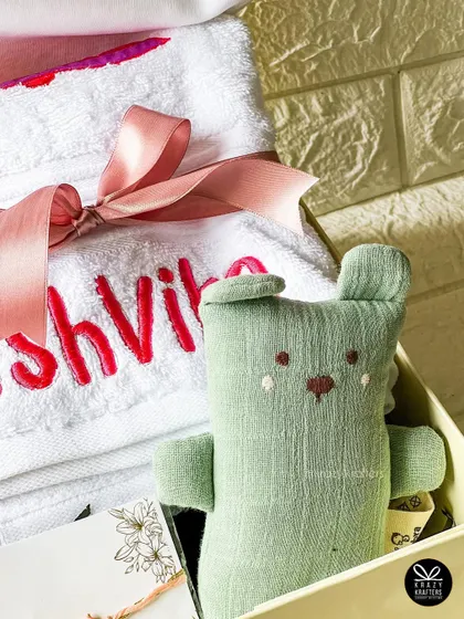 A personalized towel with the name 'Tashvika' embroidered in bright pink, paired with a soft green bear toy for a special Rakhi gift.