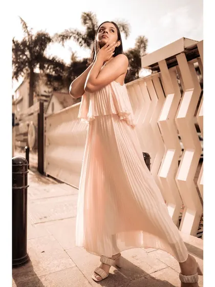 Model in a pink pleated dress posing with hands framing her face, in a sepia-toned street photo