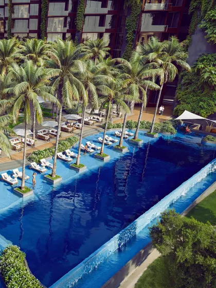 The infinity pool at the upcoming Westin Nashik, surrounded by palm trees and lush landscaping. The design aims to create a seamless transition from the built environment to the natural waterfront, offering a truly immersive resort experience.