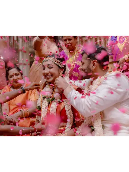 A joyous moment from a South Indian wedding, with the couple showered in pink rose petals by their family and friends.
