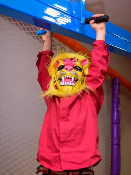 Roar! A child in a fierce lion mask hangs from the monkey bars in our play zone, embracing his wild side.