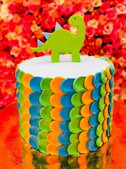 This dinosaur cake features a colorful 'dinosaur scale' piping technique on the side and a simple green dinosaur topper. It's a creative and eye-catching design.