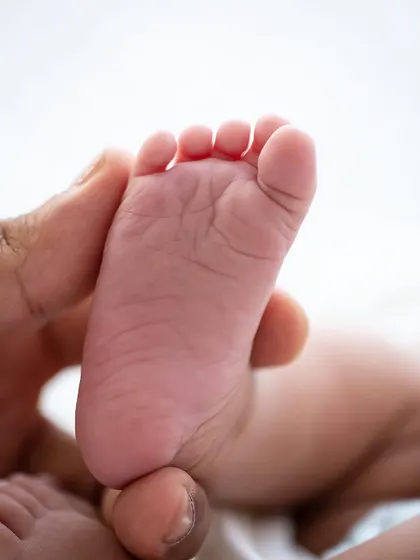 A parent's thumb gently holds a tiny foot, showing the incredible scale and sweetness of a newborn's features.