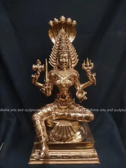 A polished bronze sculpture of Mariamman, with the five-headed cobra hood rising above her crown. She holds a trident and drum, symbols of her power to protect and create.