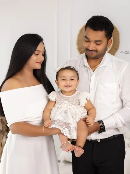 A sweet family portrait with the parents looking lovingly at their baby girl. The simple, bright background keeps the focus on their connection.