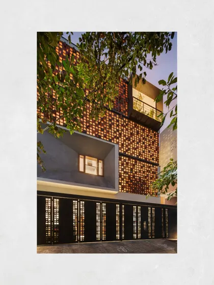 A dramatic evening shot of the Kamala Residence, where the illuminated facade highlights the texture of the breeze blocks and the depth of the projecting window.