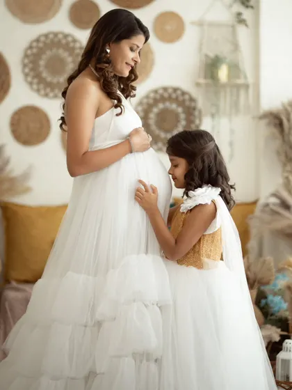 A tender moment as a young girl kisses her mother's baby bump, a perfect way to include siblings in the maternity shoot.