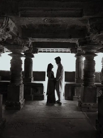 A dramatic black and white silhouette of a couple inside a temple corridor. The strong pillars and contrasting light create a powerful and timeless image.