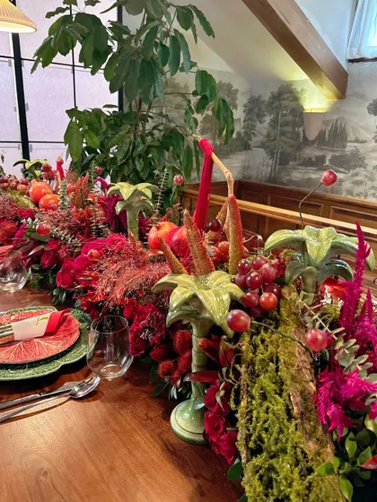 The full length of the harvest-style table runner, abundant with red florals, fruits, and greenery, creating a feast for the eyes.