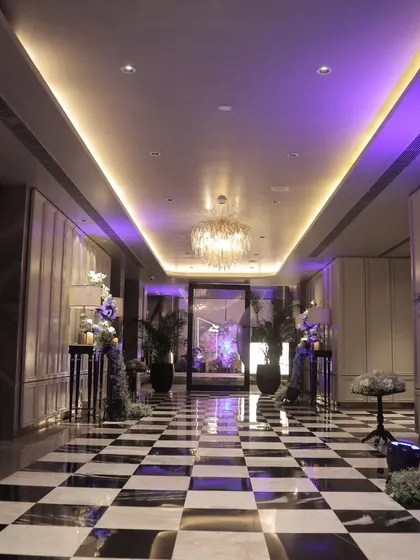 A stylish entryway with a black-and-white checkered floor, leading into an event space. The corridor is elegantly styled with floral arrangements and console tables, setting a sophisticated tone from the moment guests arrive.