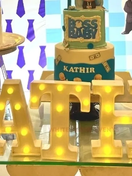 A close-up of the personalized details at a Boss Baby party, showing the birthday boy's name in lit-up marquee letters in front of a themed cake.
