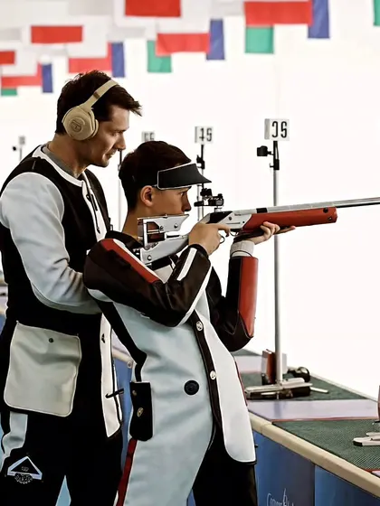 Precision meets guidance. A coach provides hands-on instruction to a young shooter, ensuring every detail of his stance and grip is perfect.