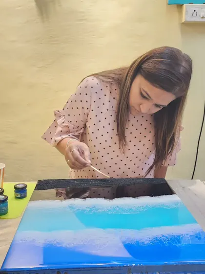 Concentration and creativity in action. A student carefully works on her ocean art piece, using a tool to create delicate wave patterns in the resin.