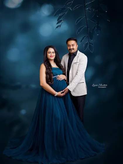 A beautiful couple's portrait in a moody, artistic setting. The deep teal gown and the husband's embrace create a romantic and enchanting scene.