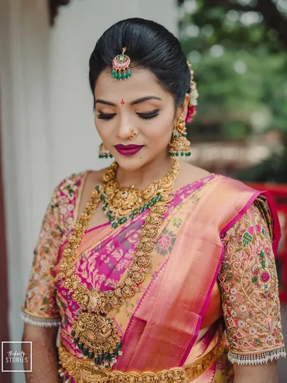 A quintessential bridal portrait of a bride in a pink and gold saree, her makeup and temple jewelry looking flawless.