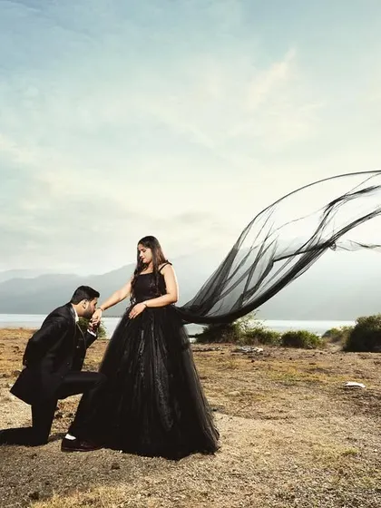 A dramatic pre-wedding shot at Tehri lake, with the groom kissing the bride's hand as her black gown flows in the wind. This image has a grand, cinematic feel.