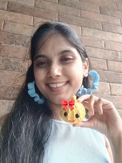Me holding a cute crochet Modak I made for a contest, while wearing my handmade blue crochet hoop earrings.