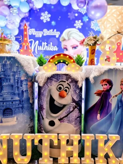 A magical 'Frozen' themed birthday party featuring custom-printed pedestals with characters like Elsa, Anna, and Olaf, marquee letters, and a winter wonderland backdrop.