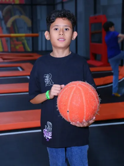 Holding a basketball, this young athlete is ready for some high-flying action in our trampoline basketball zone.
