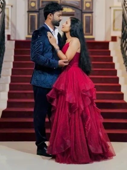 A close-up, romantic shot of the couple. You can see the texture of his blue velvet suit and the delicate straps of her red ruffled gown, a perfect pairing.