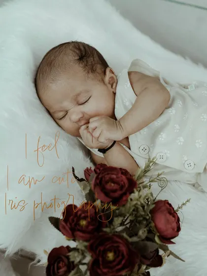 A peaceful and delicate newborn portrait of a baby sleeping soundly on a soft, white fur blanket. The simple setup with a touch of floral decoration emphasizes the innocence and beauty of a newborn's first days.
