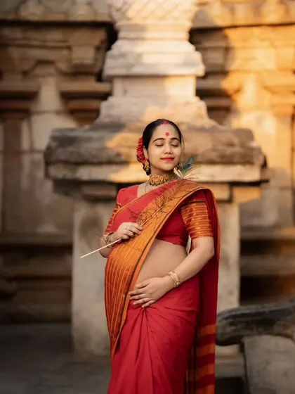 A serene portrait of the mother-to-be holding a peacock feather, a symbol of grace and beauty, amidst the temple's stunning architecture.