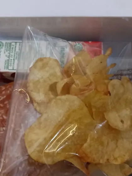A burger and bag of potato chips are packed with a drink and sweet in this snack box we show open.