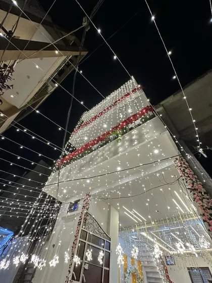 The exterior of a multi-story house completely covered in drapes and fairy lights for a wedding. The scale of the decoration is grand and impressive.